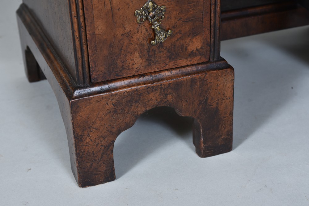 An antique burr walnut kneehole bureau featuring a slant-front writing slope, brass drop handles, and bracket feet. View VIII
