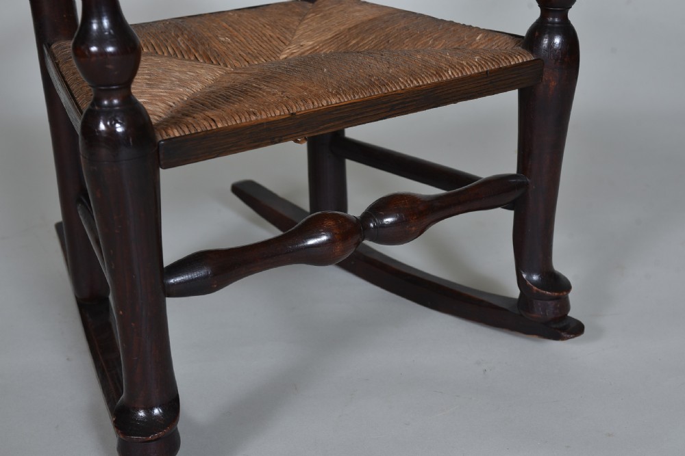 An early nineteenth-century childs rocking chair crafted from dark brown wood with a shaped ladderback backrest, turned armrests, and a woven rush seat. View VII