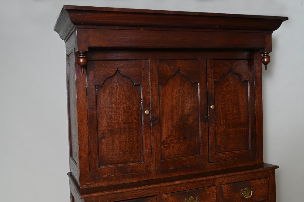 An 18th-century dark oak Welsh press cupboard featuring upper ogee arched panel doors, turned drop finials, three middle drawers, and a double-door base. View II
