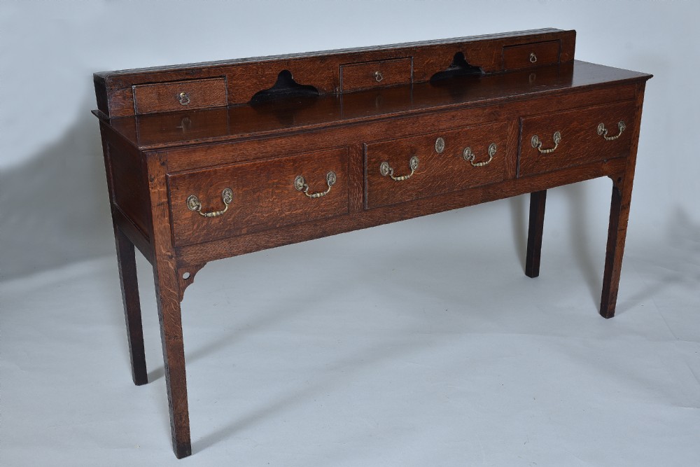 An 18th-century oak dresser base featuring three main drawers with brass handles and a low raised gallery containing three small drawers and two arched alcoves.