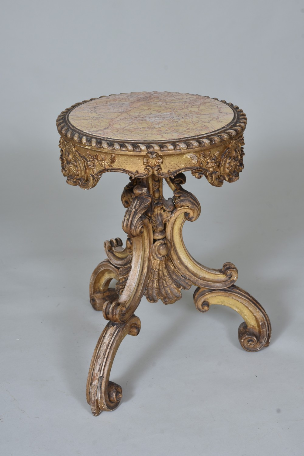 A 19th-century circular side table featuring a mottled marble top, intricate carved giltwood apron, and a scrolled tripod support base.