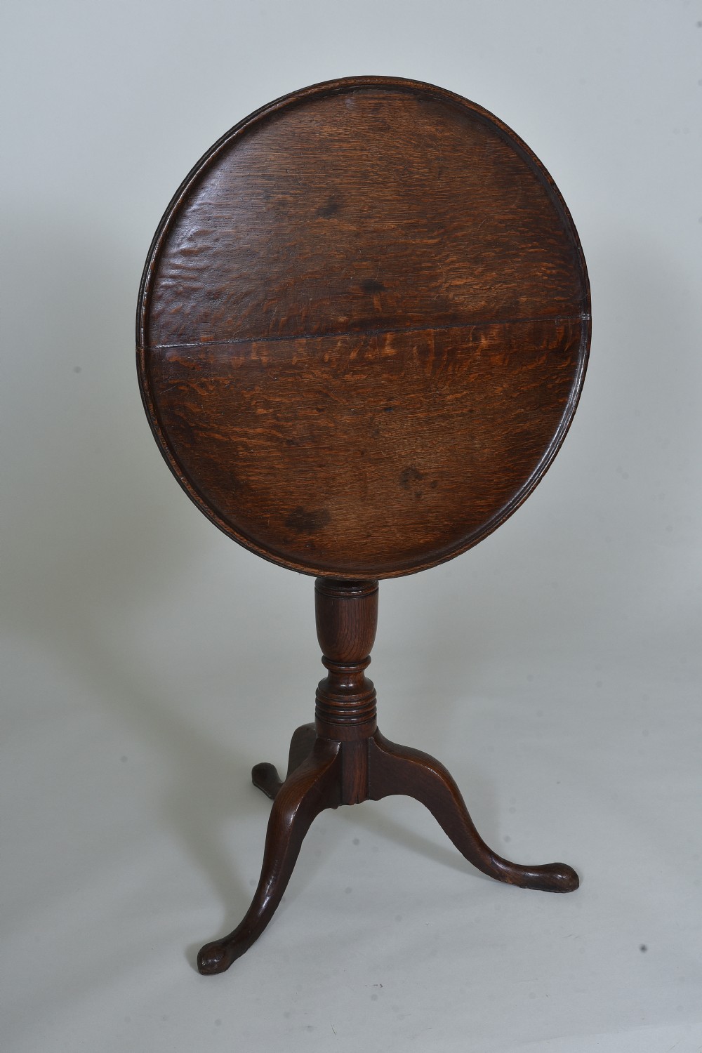 An antique dark oak tripod table with a circular tilt-top resting vertically on a turned central pedestal with three splayed legs.
