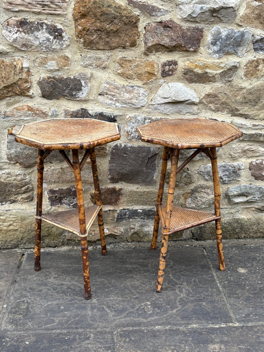 A pair of antique bamboo side tables featuring octagonal woven cane tops, triangular undertiers, and mottled brown bamboo legs.