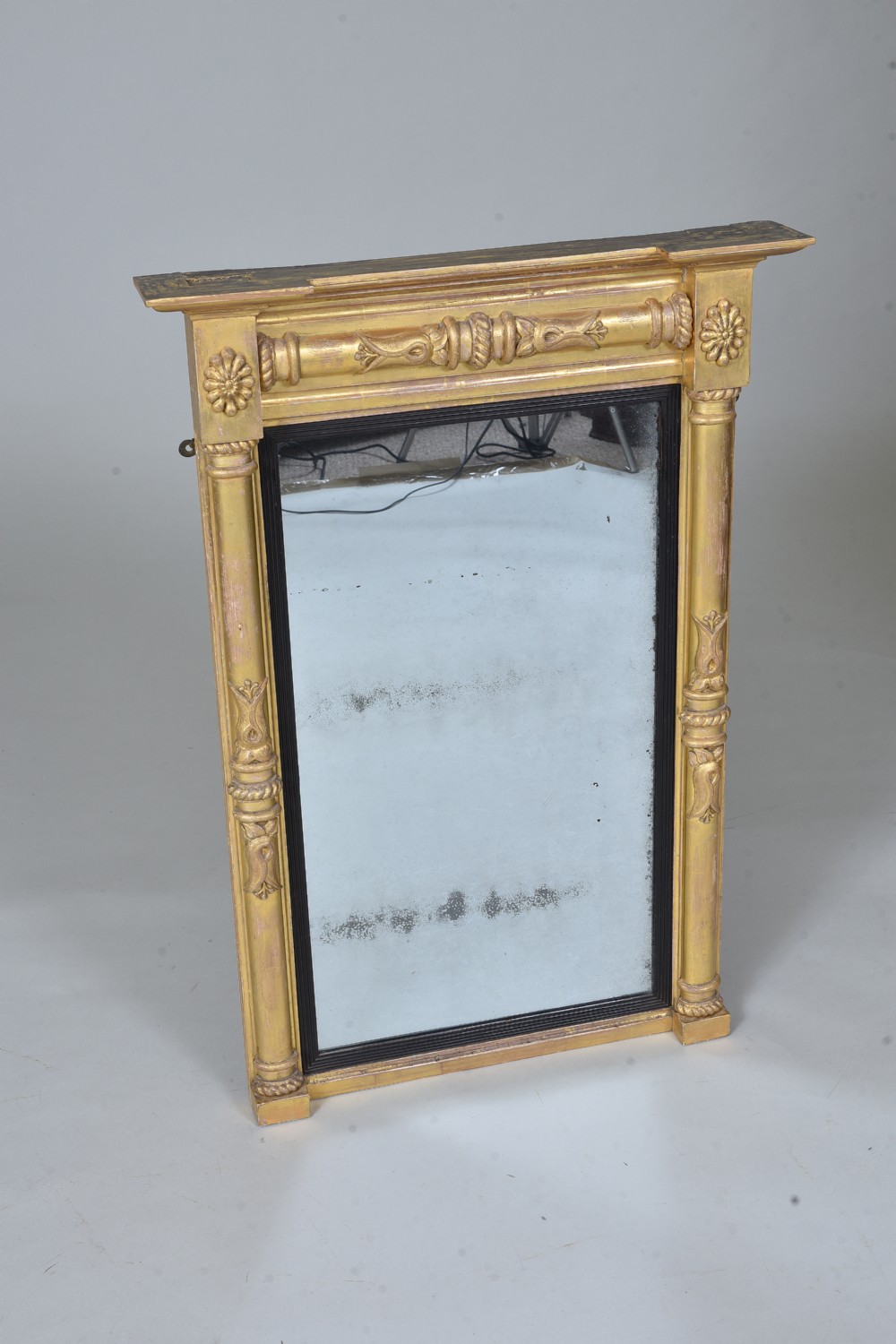 A rectangular Regency giltwood wall mirror featuring side columns, rosette medallions, an ornamental frieze, and an ebonised inner slip.