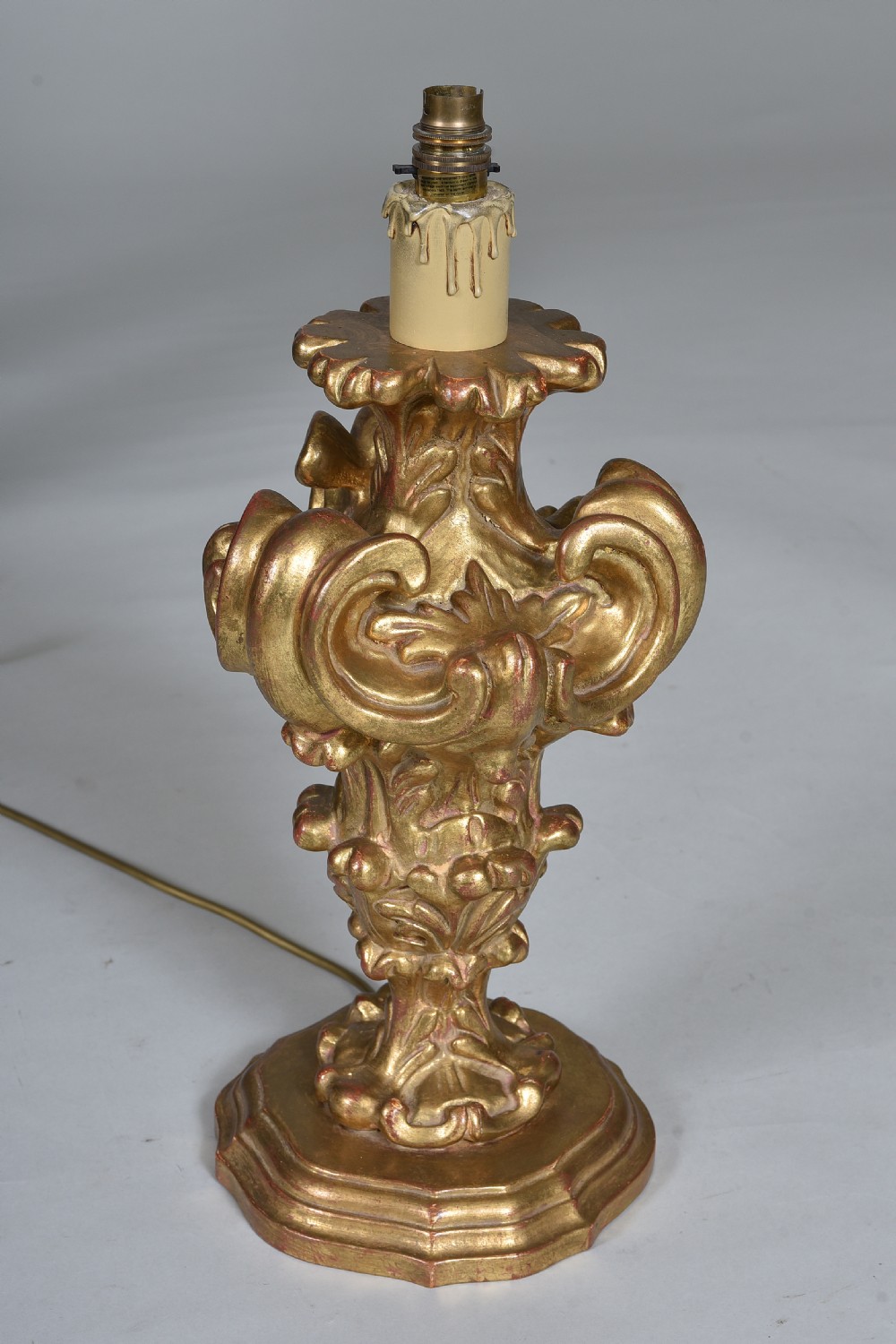 An antique carved giltwood table lamp base featuring scrollwork, acanthus leaf motifs, and a cream faux-candle fitting at the top.