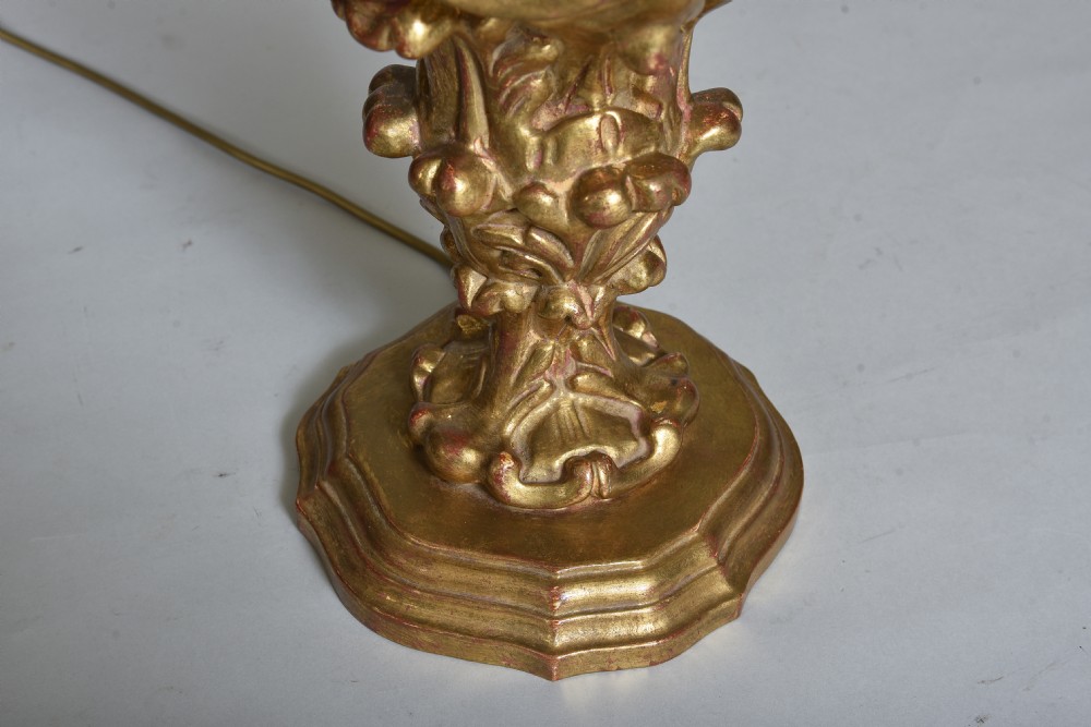 An antique carved giltwood table lamp base featuring scrollwork, acanthus leaf motifs, and a cream faux-candle fitting at the top. View VI