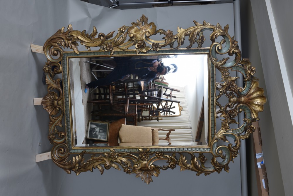 An ornate rectangular wall mirror featuring an elaborate carved giltwood frame decorated with shell motifs, acanthus leaf flourishes, and subtle teal painted accents. View V