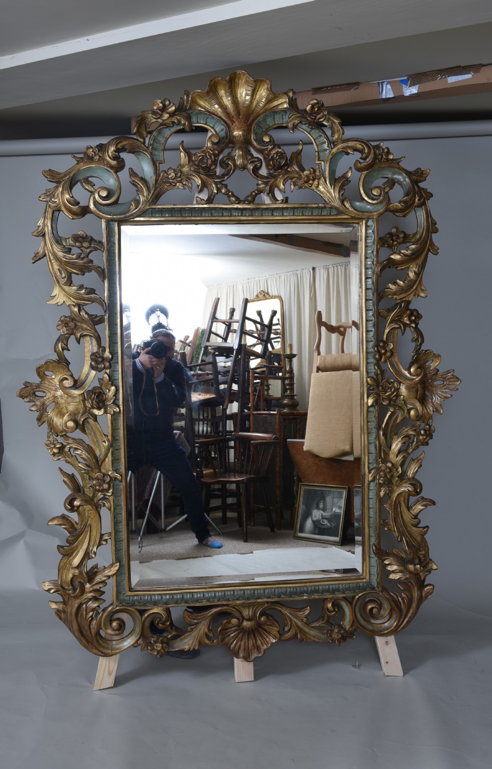 An ornate rectangular wall mirror featuring an elaborate carved giltwood frame decorated with shell motifs, acanthus leaf flourishes, and subtle teal painted accents. View VI