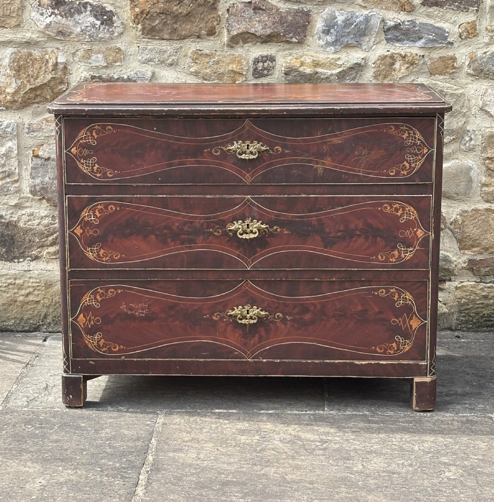 A three-drawer dark red painted wooden chest featuring gold filigree scrollwork, faux grain detailing, and ornate brass drop handles. View III