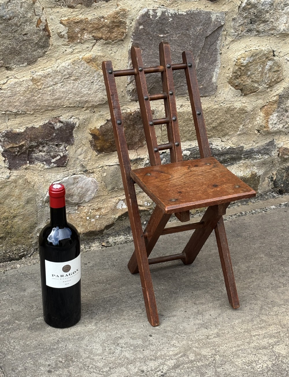 A dark brown wooden folding childs chair featuring an X-frame construction, a flat rectangular seat, and a slatted backrest with metal fixings. View III