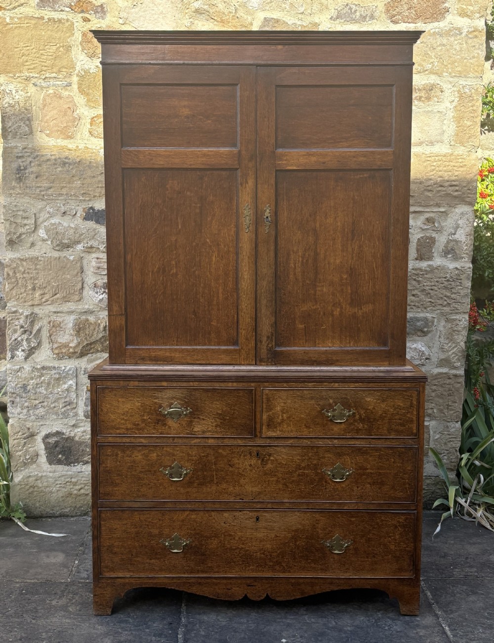 An 18th-century dark oak cupboard on chest featuring paneled upper doors, lower drawers with brass handles, and a moulded cornice. View VII