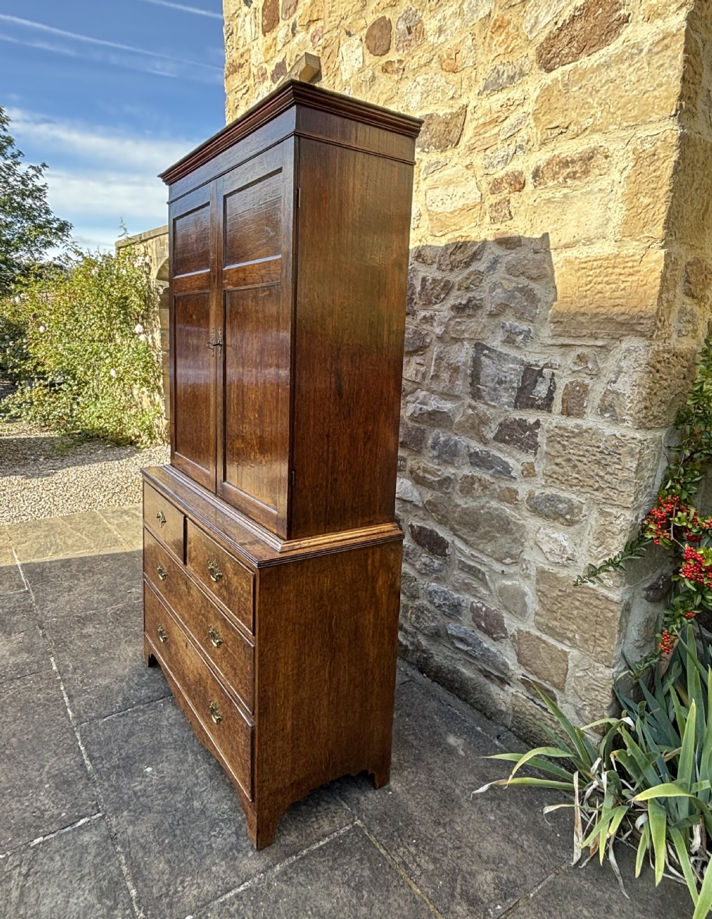 An 18th-century dark oak cupboard on chest featuring paneled upper doors, lower drawers with brass handles, and a moulded cornice. View X