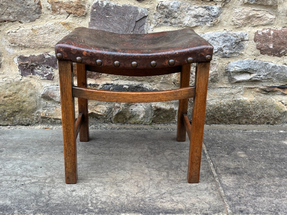 An Edwardian stool constructed from dark oak featuring a curved leather saddle seat secured with metal studs. View IV