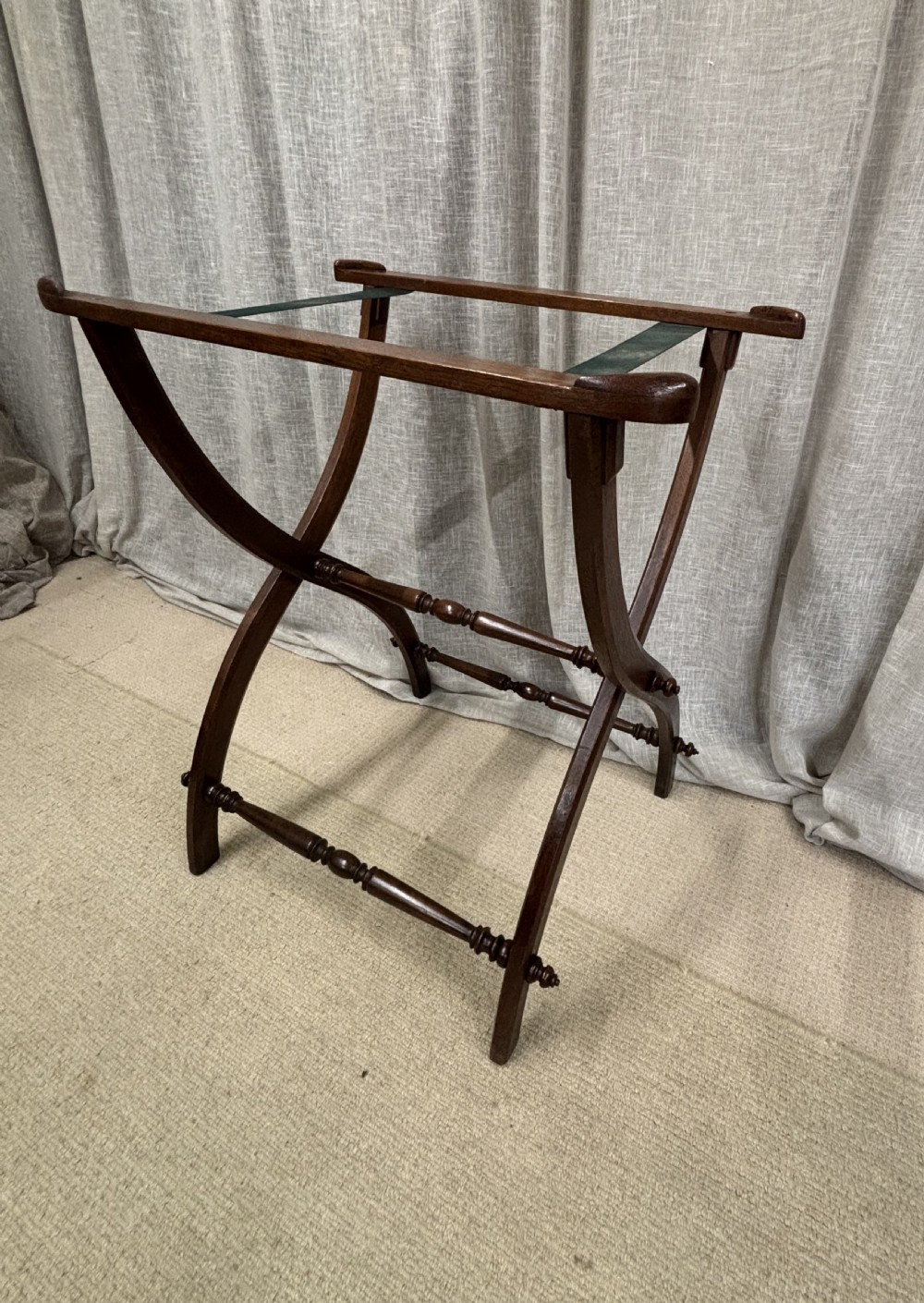 An antique dark oak oval butlers tray with carved edge detailing resting on a matching folding stand with curved legs and turned stretchers. View II