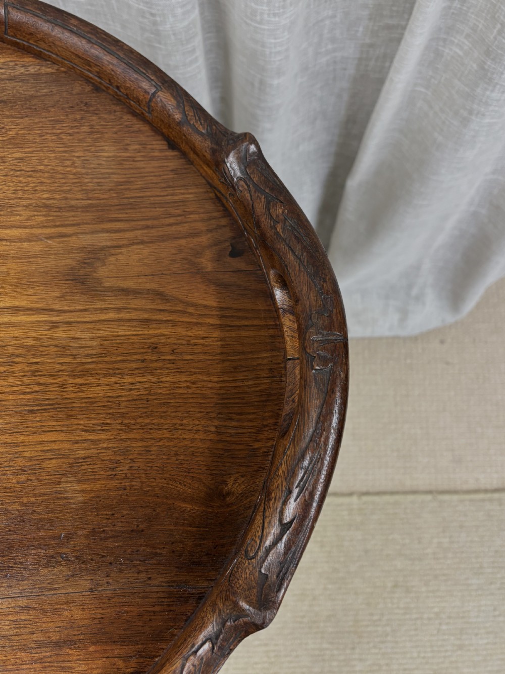 An antique dark oak oval butlers tray with carved edge detailing resting on a matching folding stand with curved legs and turned stretchers. View III
