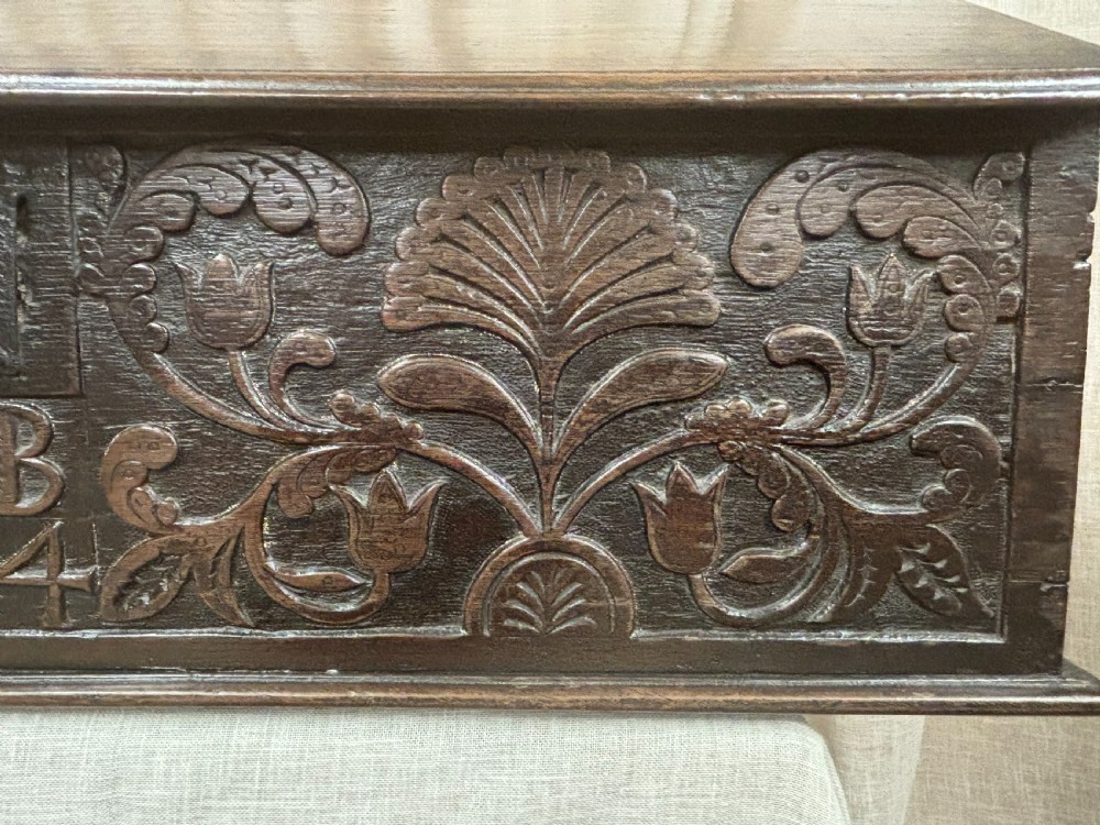A dark carved oak desk box featuring a sloped lid, iron hinges, and a front panel carved with relief floral patterns, the initials M B, and the date 1724. View III