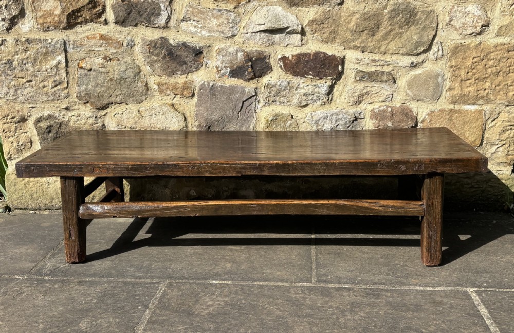 An antique low rectangular coffee table crafted from dark patinated elm wood with thick legs and sturdy stretchers.
