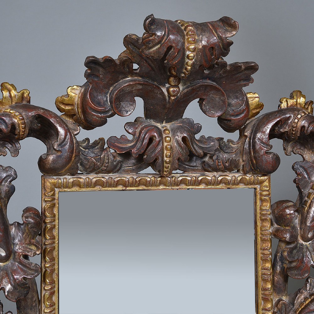 An ornate Italian carved wood wall mirror with elaborate acanthus leaf cresting and C-scroll motifs finished in gold and silver leafing around a central glass plate. View II