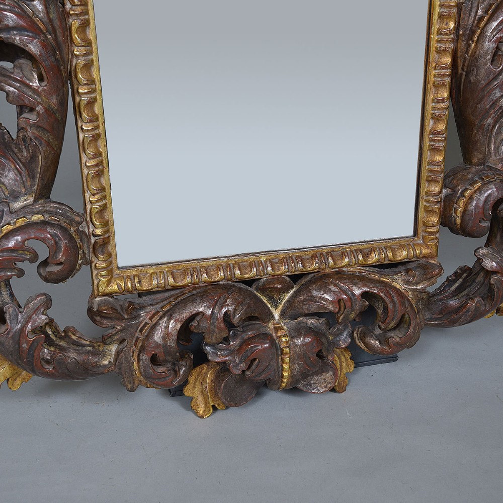 An ornate Italian carved wood wall mirror with elaborate acanthus leaf cresting and C-scroll motifs finished in gold and silver leafing around a central glass plate. View III