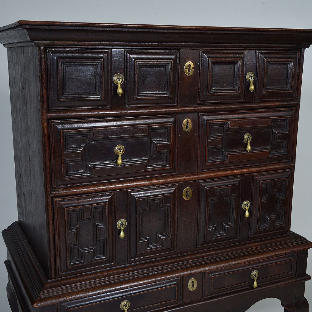 A dark oak chest on stand with geometric panelled drawers, brass drop handles, and cabriole legs. View II