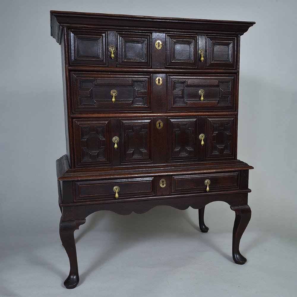 A dark oak chest on stand with geometric panelled drawers, brass drop handles, and cabriole legs. View III