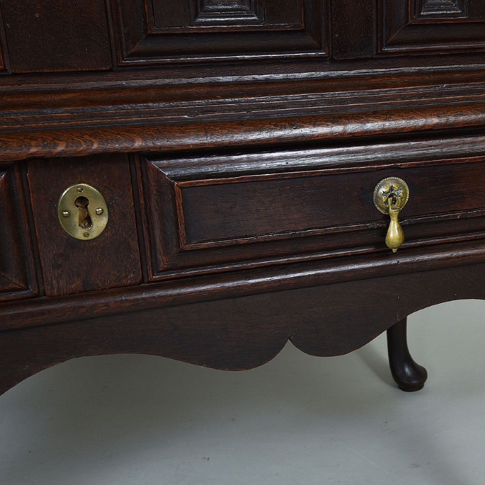 A dark oak chest on stand with geometric panelled drawers, brass drop handles, and cabriole legs. View IV