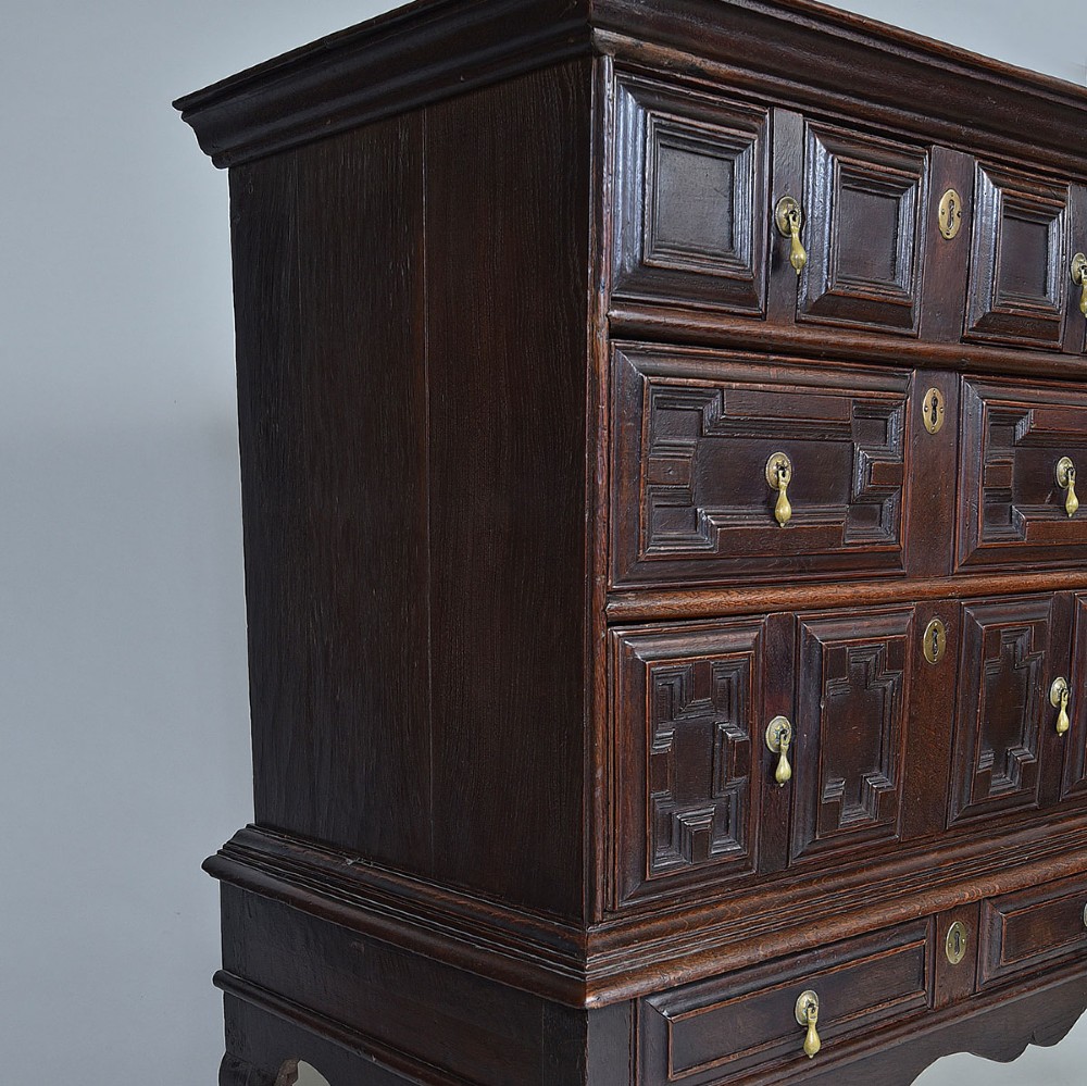 A dark oak chest on stand with geometric panelled drawers, brass drop handles, and cabriole legs. View VI