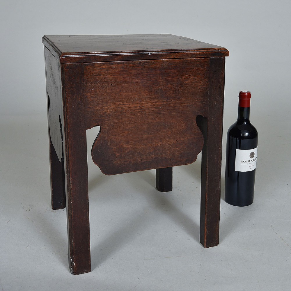 An early nineteenth-century dark mahogany box stool featuring a flat top lid, square legs, and decorative shaped aprons.