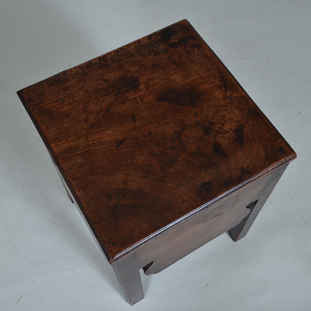 An early nineteenth-century dark mahogany box stool featuring a flat top lid, square legs, and decorative shaped aprons. View II