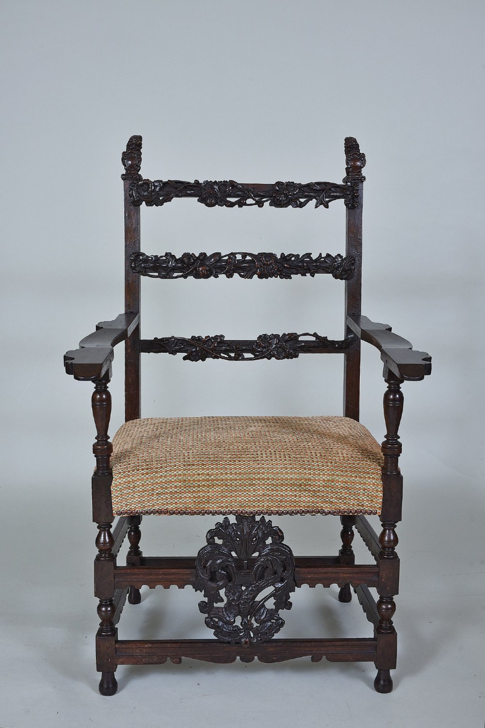 An 18th-century Italian dark walnut armchair featuring intricate openwork foliage carving across the back rails and front stretcher, turned supports, and a patterned woven seat.