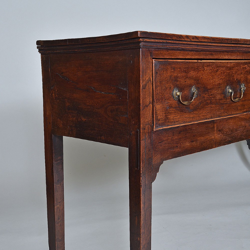 An 18th-century warm brown elm dresser base featuring three drawers with brass drop handles and square legs. View III