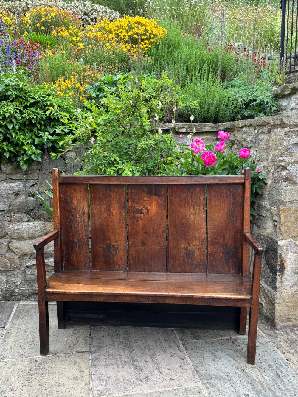 An 18th-century oak settle with a high panelled backrest, flat armrests, and straight legs.