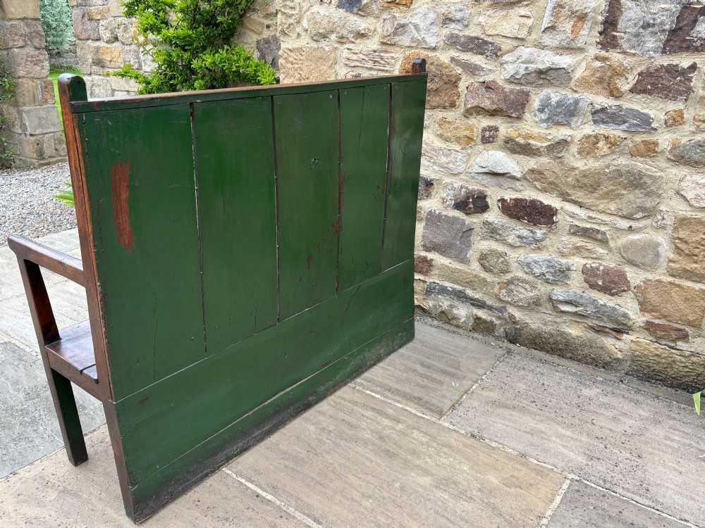 An 18th-century oak settle with a high panelled backrest, flat armrests, and straight legs. View V