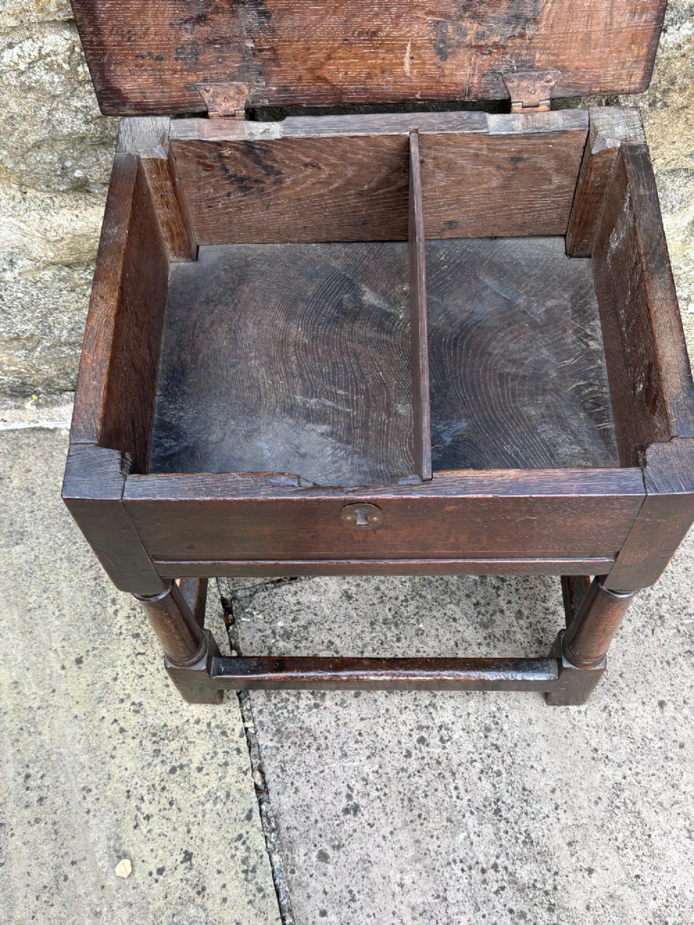 A dark oak 17th-century box stool featuring a flat hinged rectangular lid, a keyhole on the front apron, turned legs, and lower wooden stretchers. View V