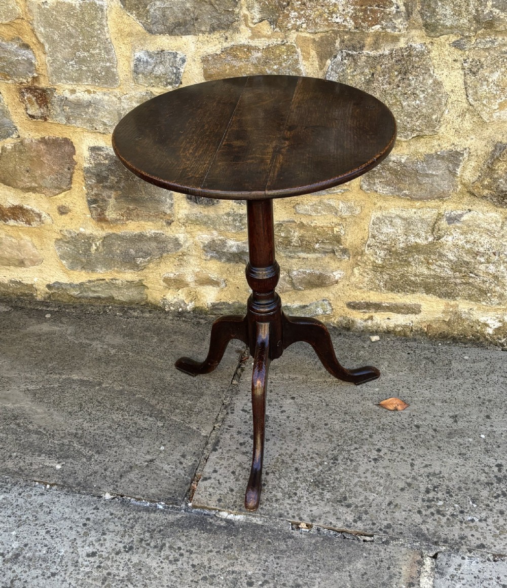 An 18th-century dark oak tripod table featuring a circular top, turned central pedestal stem, and three splayed legs.