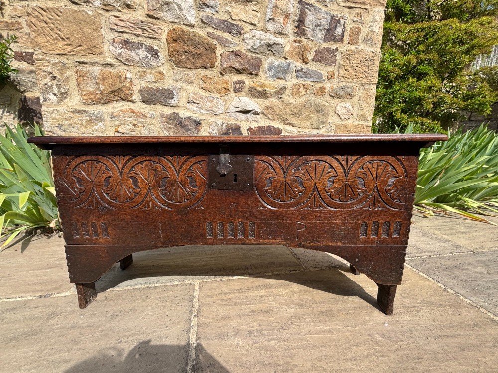 A 17th-century carved oak coffer featuring relief lunette carvings, an iron lockplate, and a dark polished timber finish. View IV