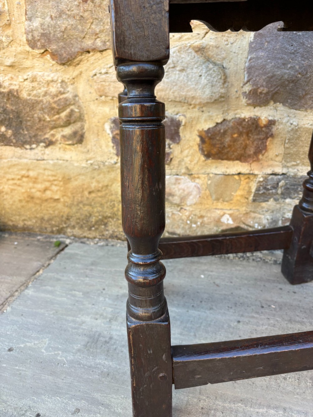 A 17th-century dark oak joint stool featuring turned legs, pegged mortise and tenon joinery, a carved frieze, and a plain rectangular wooden seat. View II