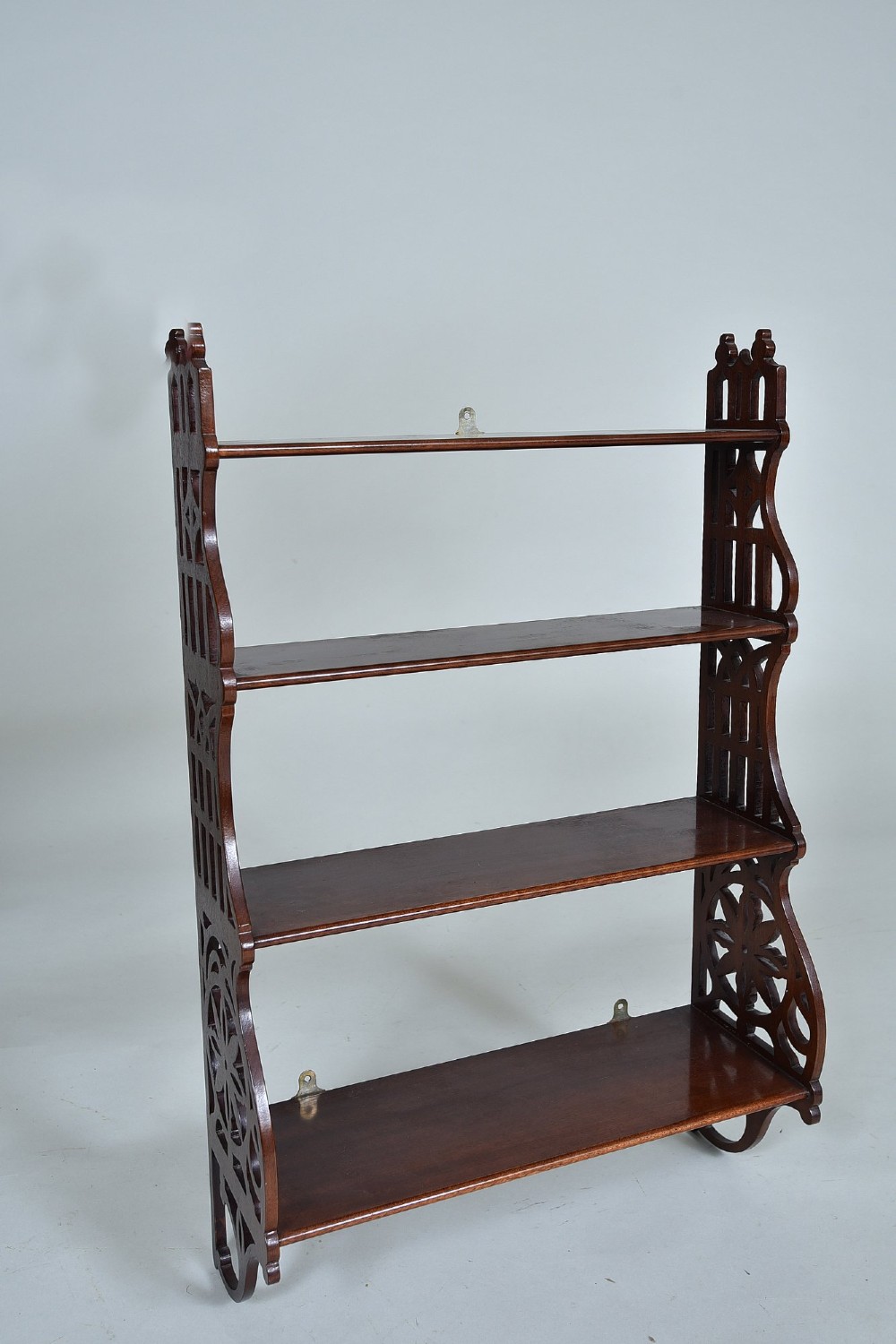 A four-tier mahogany wall shelf featuring open pierced fretwork sides with Gothic-style tracery and brass mounting brackets.