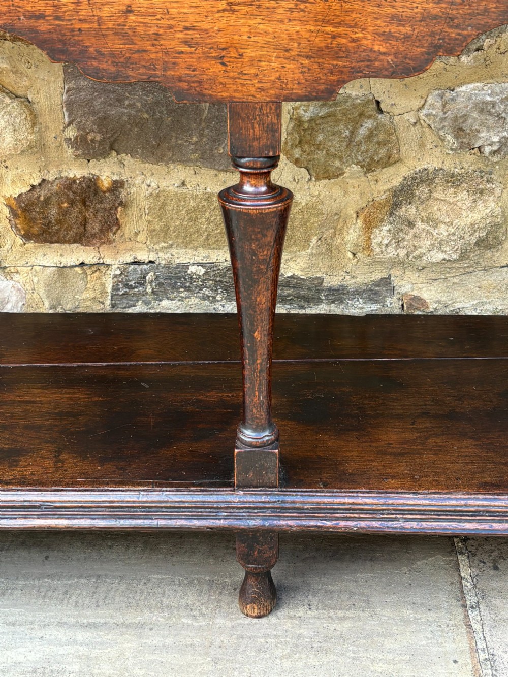 An 18th-century dark oak dresser base featuring two drawers with brass handles, a shaped apron, turned front legs, and a lower potboard shelf. View IV