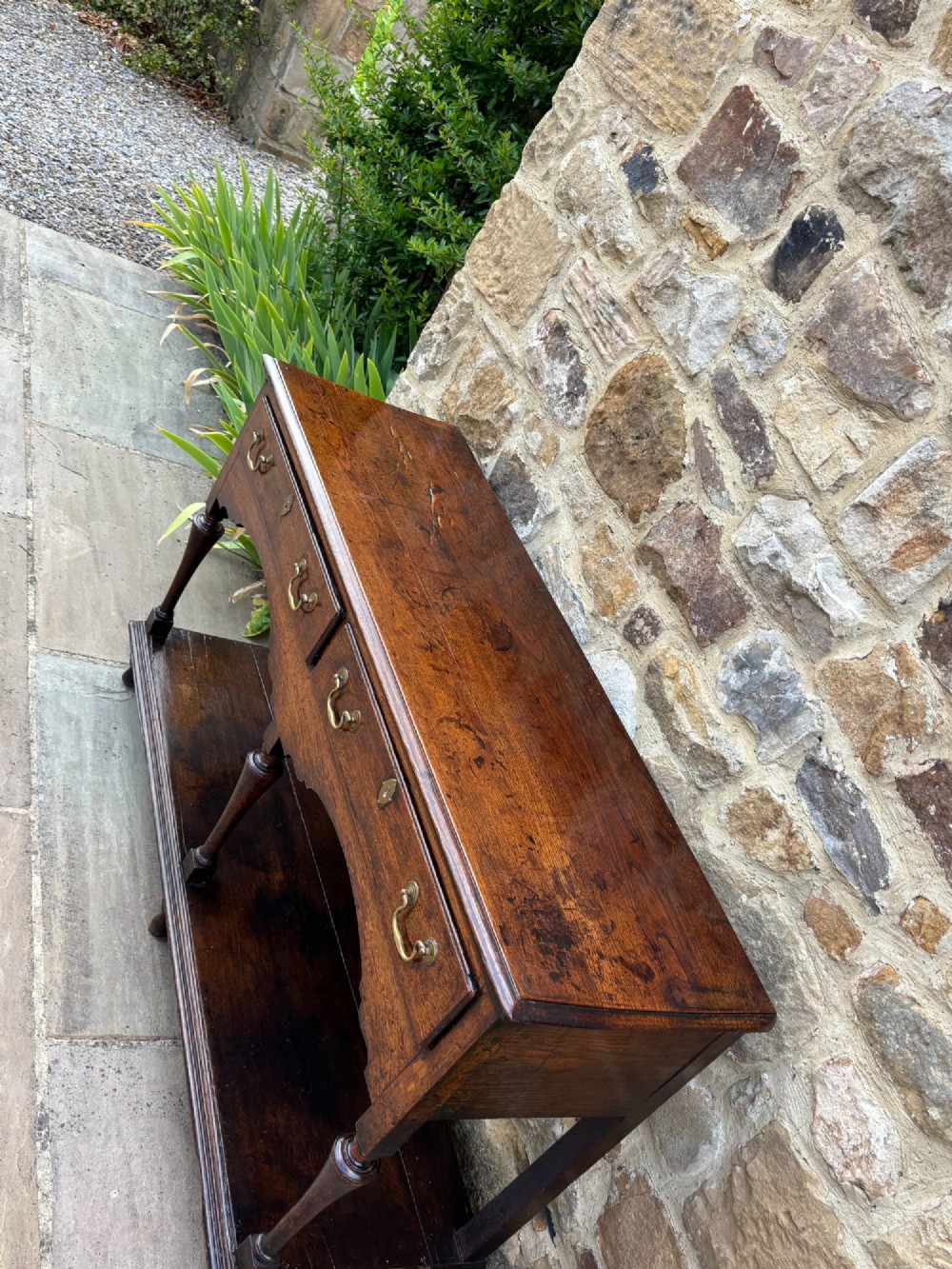 An 18th-century dark oak dresser base featuring two drawers with brass handles, a shaped apron, turned front legs, and a lower potboard shelf. View V