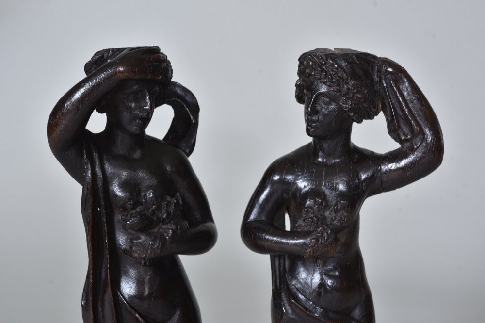 A pair of dark carved oak figures depicting classical drapery-clad subjects standing on carved square pedestals. View II