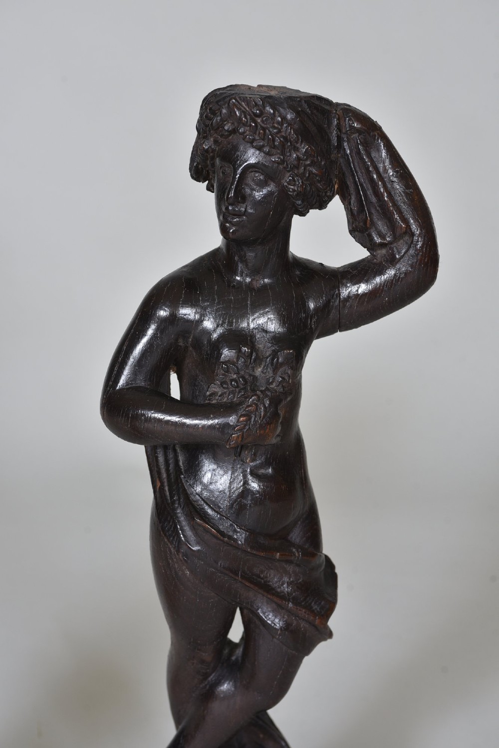 A pair of dark carved oak figures depicting classical drapery-clad subjects standing on carved square pedestals. View V
