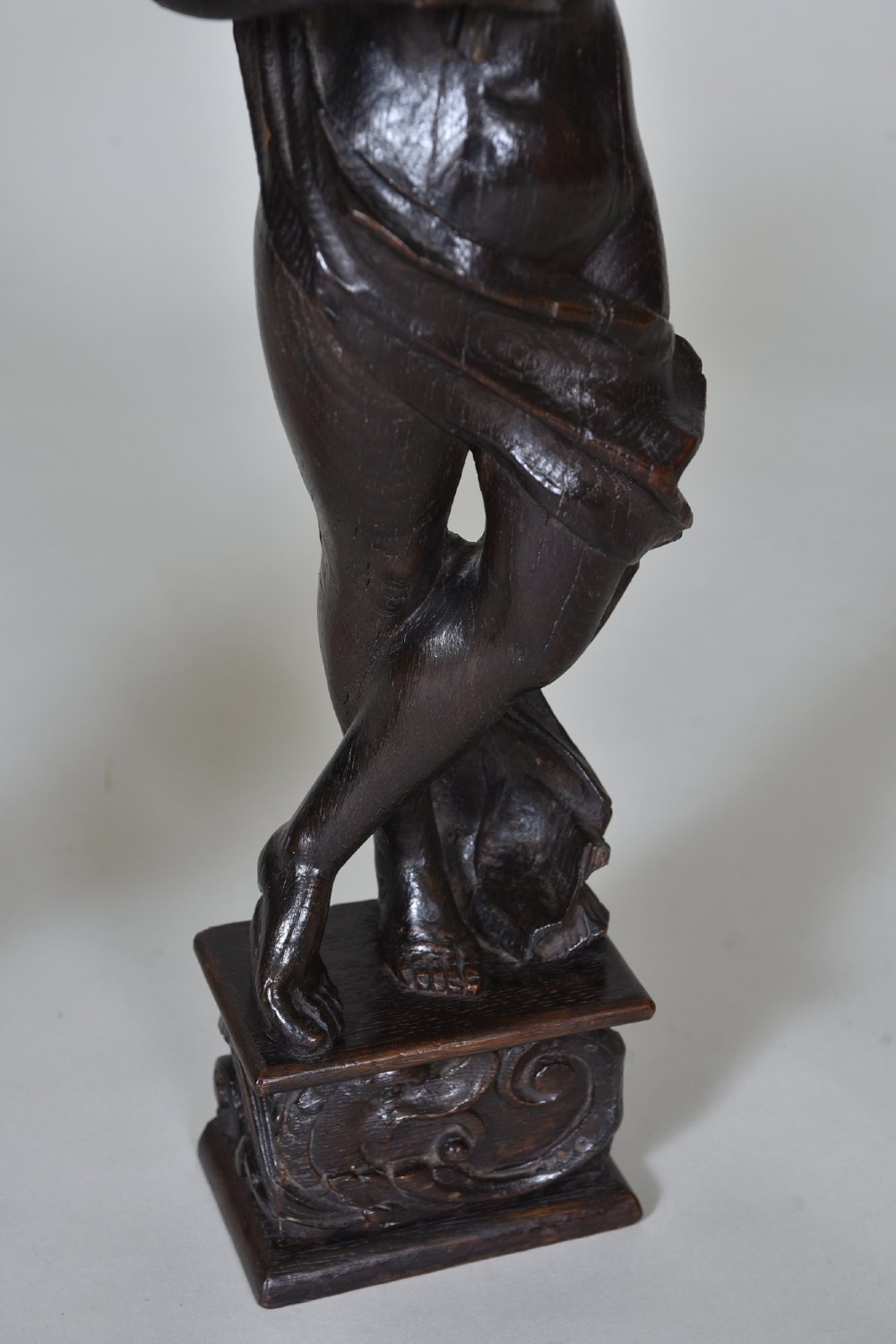 A pair of dark carved oak figures depicting classical drapery-clad subjects standing on carved square pedestals. View VI