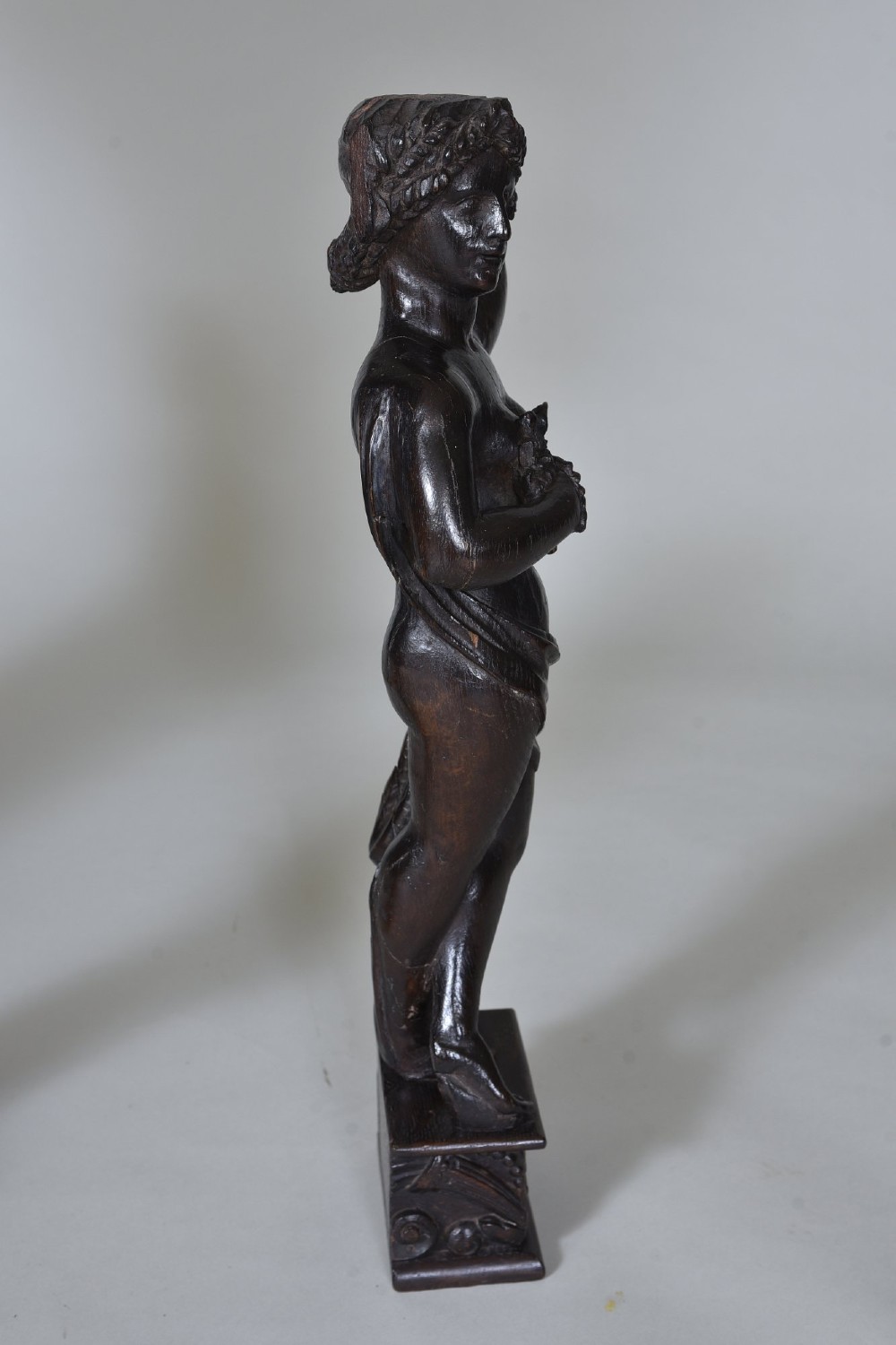 A pair of dark carved oak figures depicting classical drapery-clad subjects standing on carved square pedestals. View VII