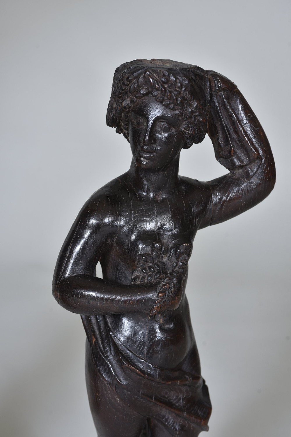 A pair of dark carved oak figures depicting classical drapery-clad subjects standing on carved square pedestals. View X