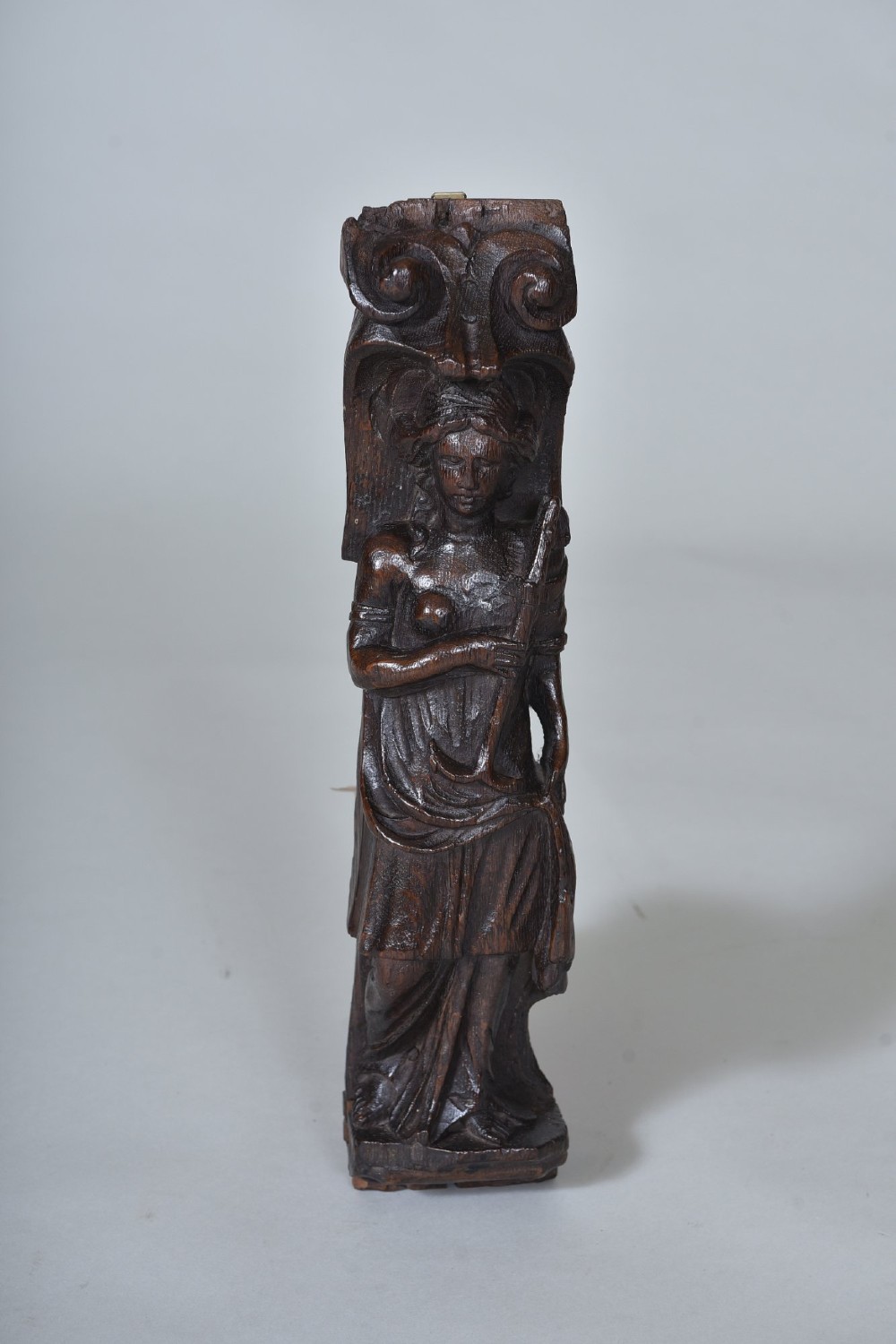 A hand-carved dark oak figure depicting a draped female holding an anchor beneath a scroll volute capital.