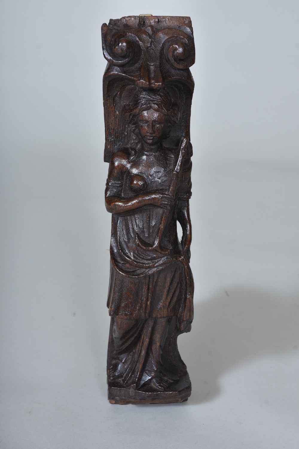 A hand-carved dark oak figure depicting a draped female holding an anchor beneath a scroll volute capital. View II