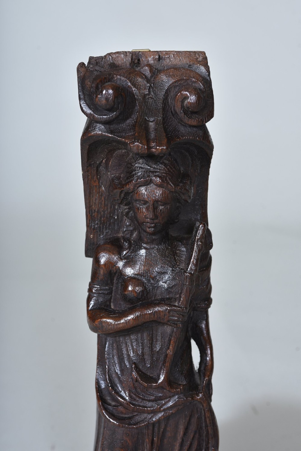 A hand-carved dark oak figure depicting a draped female holding an anchor beneath a scroll volute capital. View IV