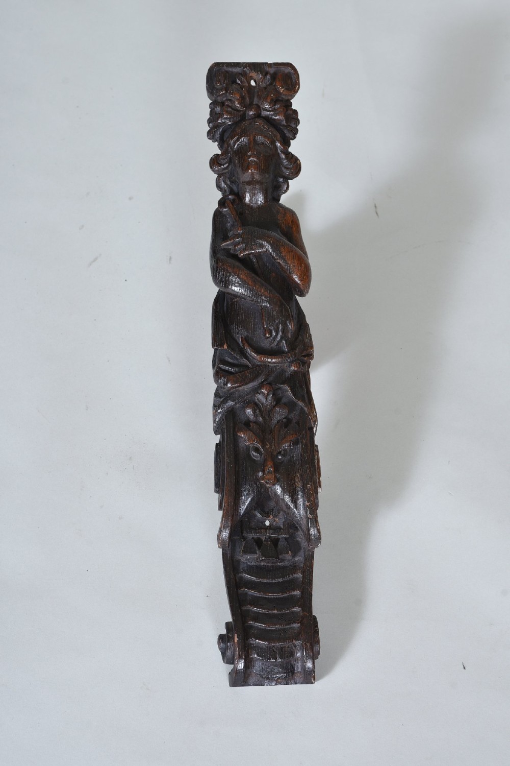 A dark oak 17th-century vertical wood carving featuring a female figure positioned above a carved grotesque mask. View II