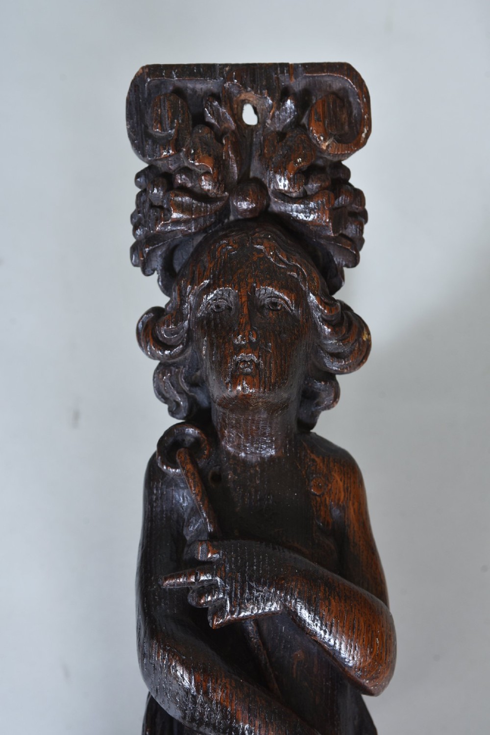 A dark oak 17th-century vertical wood carving featuring a female figure positioned above a carved grotesque mask. View IV